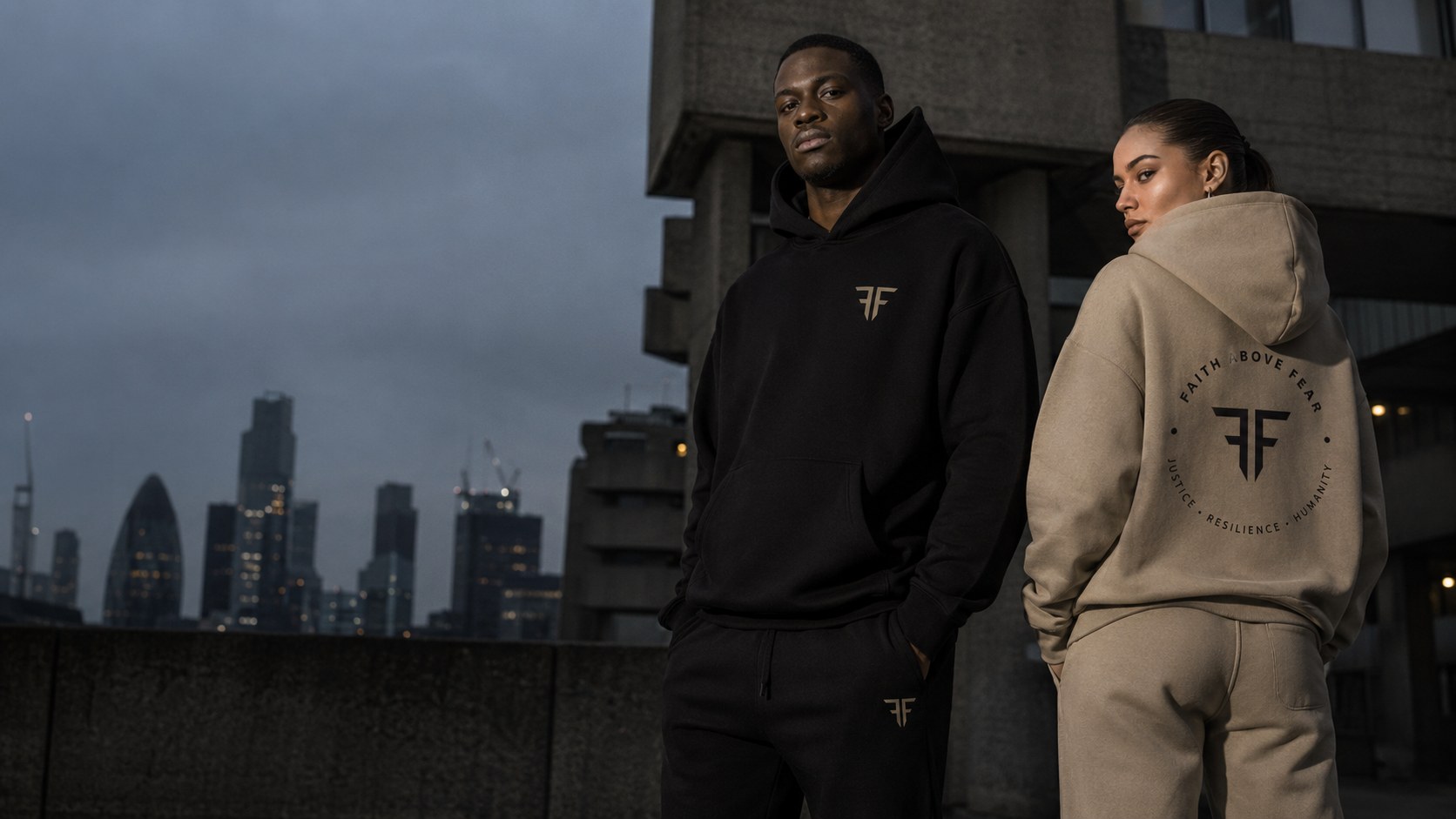Faith Above Fear campaign — two models in the black and stone sets against the city skyline at dusk